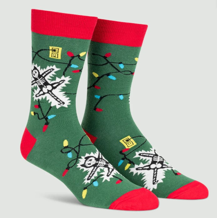 Green socks with red tops and cuffs featuring skeletons and Christmas lights on a light gray background.