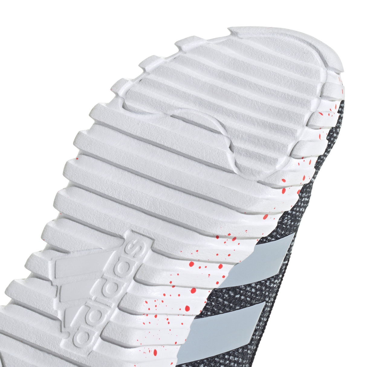 Close-up of Adidas sneaker sole with white tread pattern and red specks.