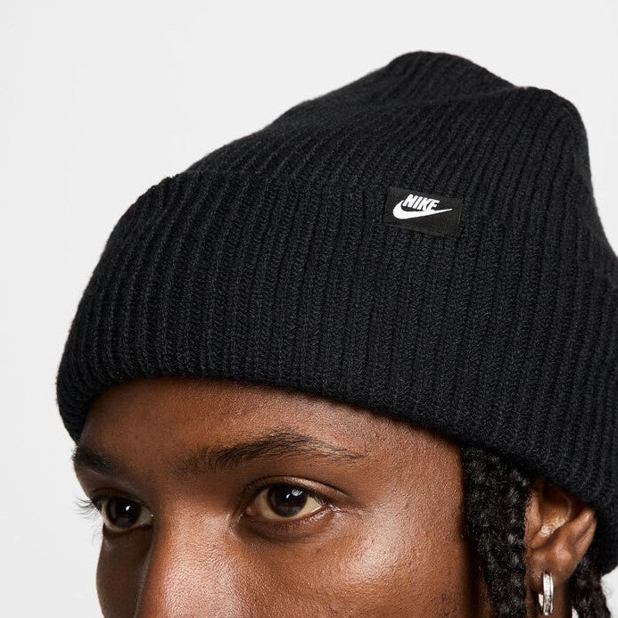 Black knit beanie with Nike logo tag worn by a person on a light gray background