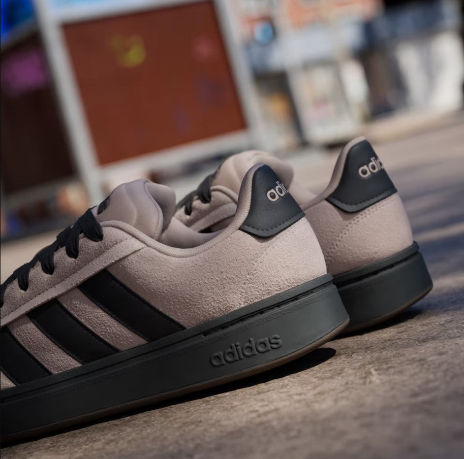 Beige Adidas sneakers with black stripes on a blurred urban background