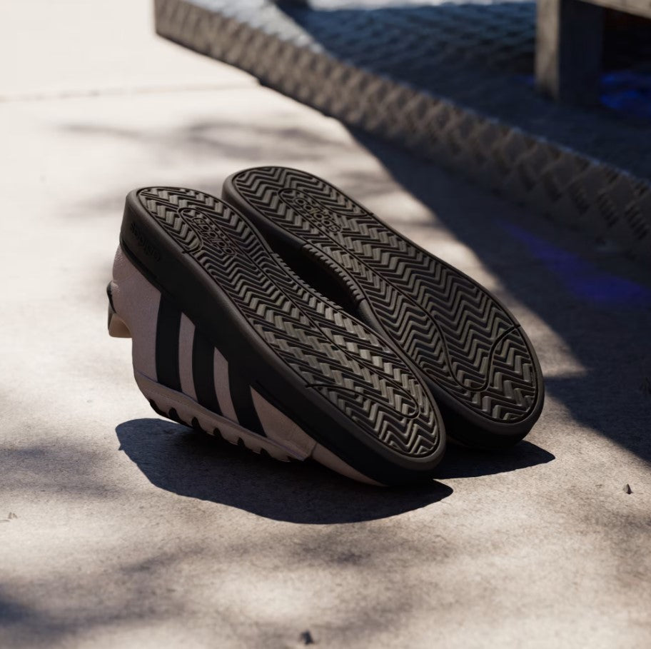 Taupe Adidias sneakers with a black textured sole on a concrete surface