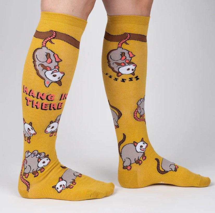 Yellow knee-high socks with possum design and text  saying 'Hang in there' on a white background