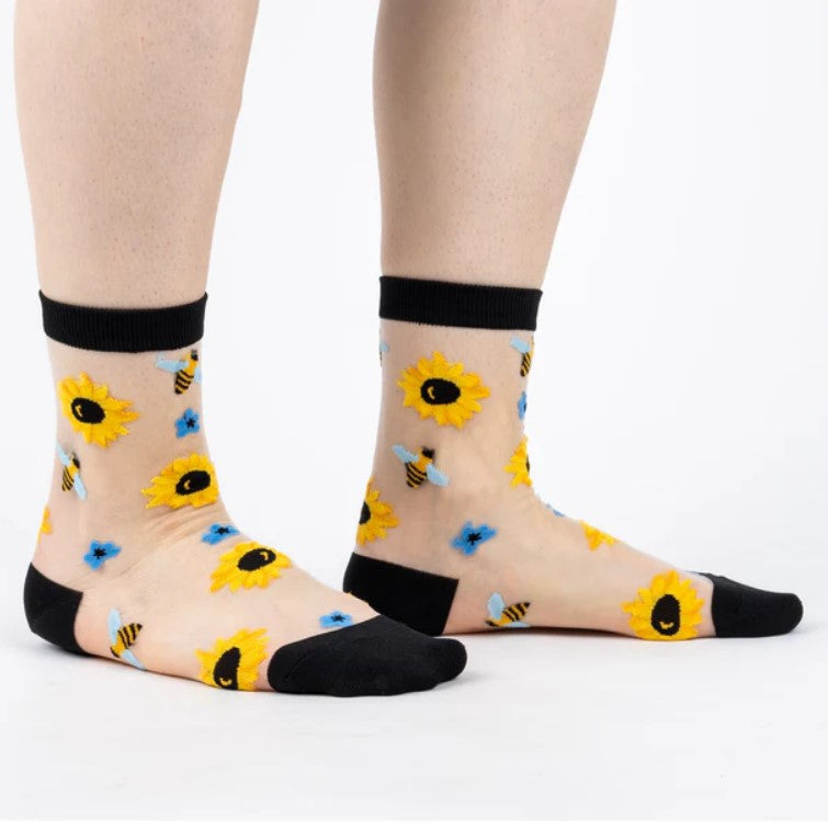 Sheer socks with sunflower and bee pattern worn by a person on a white background