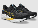 Black running shoes with yellow accents on a gray background