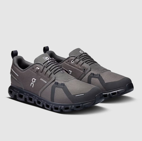 Pair of gray athletic shoes with black soles on a light gray background